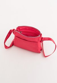 Červená nylonová taška se zipem a zápěstním popruhem. Má jednu hlavní přihrádku a vnější kapsu. Hladký povrch a kompaktní design.