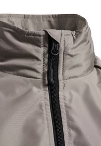 Gros plan du col d'une veste beige avec une fermeture éclair noire partiellement zippée, montrant la texture du tissu et les détails des coutures.