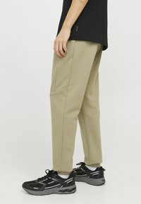 Beige sweatpants with a tapered fit, featuring side pockets and textured fabric, paired with black athletic shoes with white accents.