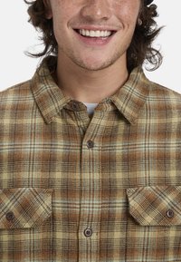 Braunes und gelbes karierte Flanellhemd mit zwei Fronttaschen und Knopfverschluss. Verfügt über eine weiche Textur und kontrastierende blaue Linien.