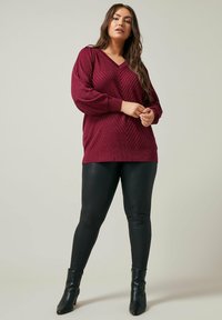 Pull en tricot bordeaux avec un col en V et un motif en chevrons texturé, associé à des leggings noirs ajustés et des bottines.