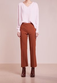 Jasnoróżowy sweter w serek, luźny krój, zestawiony z brązowymi spodniami tapered. Połyskujące ciemnobrązowe botki za kostkę z teksturą w wężowy wzór.