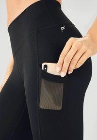 Black leggings with a side pocket, featuring a breathable mesh accent. Smooth fabric, fitted design, and subtle logo near the waistband.