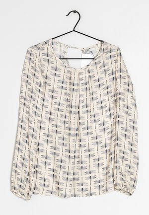 Blouse à manches longues en tissu crème avec un imprimé libellule noir. Détail du dos en clé et coupe ample avec des poignets froncés.