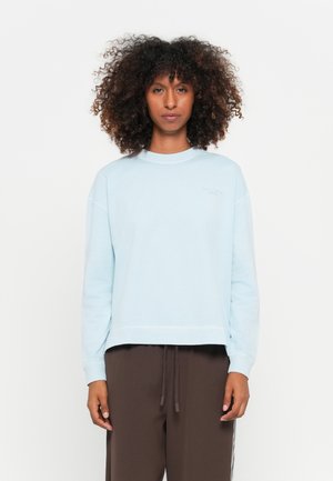 Felpa corta azzurro chiaro realizzata in tessuto morbido, con collo rotondo e spalle leggermente cadenti, abbinata a pantaloni jogger marrone scuro.