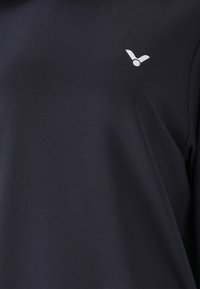 Marinblå, kortärmad skjorta gjord av slät tyg med en liten vit logotyp på övre vänstra bröstområdet.