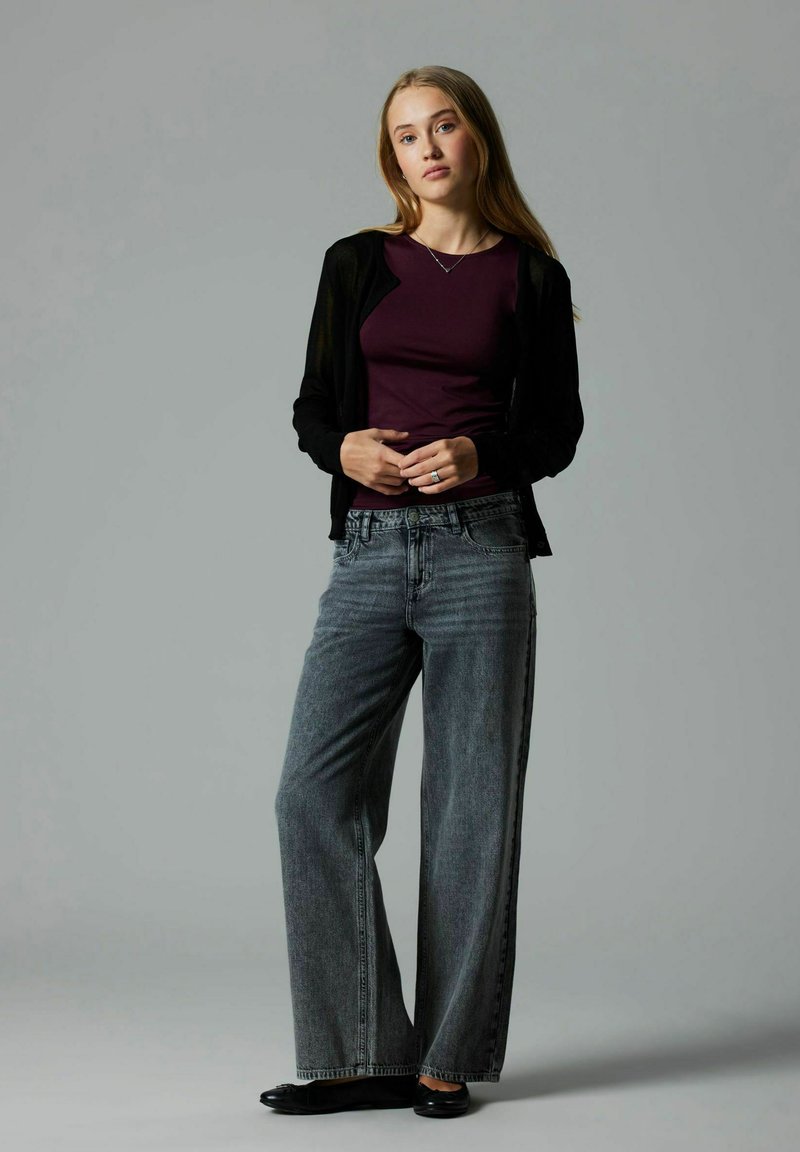 Black sheer cardigan over a dark purple top, paired with loose gray denim jeans. Outfit completed with black flat shoes. Simple and modern design.
