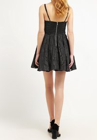 Robe noire avec des bretelles fines, corsage ajusté, jupe évasée, tissu texturé et fermeture éclair au dos.