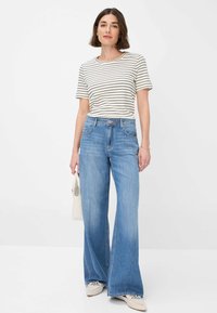 T-shirt a maniche corte a righe in crema e nero, abbinato a jeans svasati di un blu chiaro. Presenta una vita alta, cinque tasche e un orlo strappato.