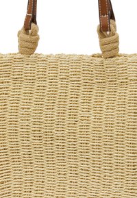 Geweven stro-tas met een beige kleur, dikke textuur en bruine leren handvatten met knoopaccenten.