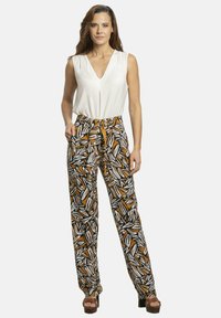 Blusa blanca sin mangas combinada con pantalones negros que presentan un patrón de hojas naranja y blanca, con cintura ajustada y un corte holgado. Sandalias de plataforma marrones.