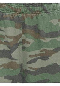 Gros plan d'un tissu avec un motif camouflage vert, marron et beige et une couture à la taille élastique.