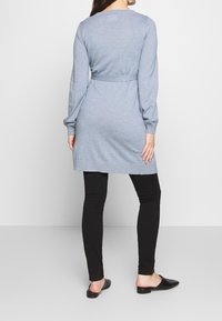 Světle modré pletené šaty s dlouhými rukávy a páskem v pase, kombinované s černými legínami a plochými černými botami. Hladká textura, ležérní design.
