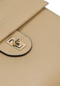 Beżowa skórzana torebka o gładkiej fakturze, z klapą składzaną i zapięciem w kolorze złotym. Krawędzie wykończone czarnymi detalami.