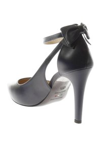 Black leather high-heeled shoe with an ankle strap and bow detail, curvy design, and tapered heel. Smooth texture with a glossy finish.