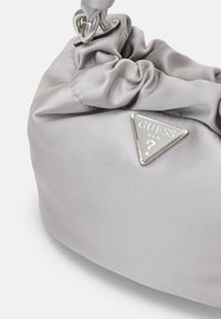 Gray satin handbag with a gathered design, featuring a silver triangular logo with "GUESS" text and a looped strap attached to a circular hardware.