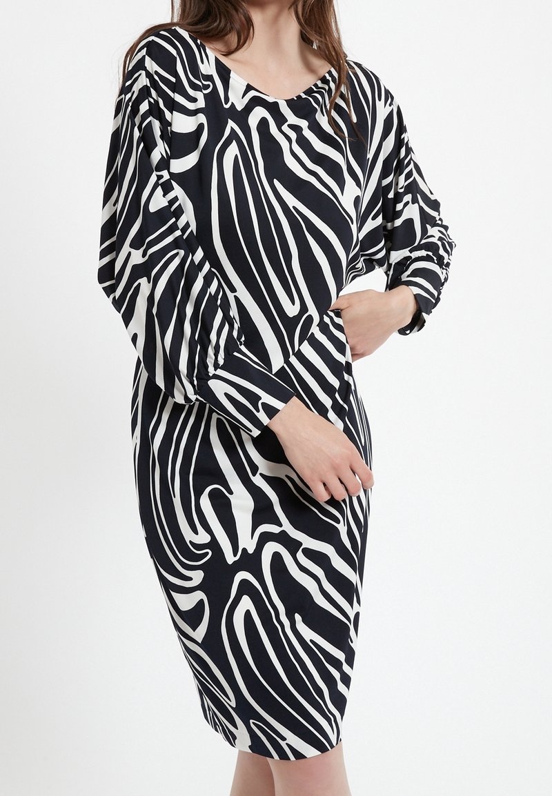 Robe noire et blanche avec un motif abstrait audacieux, manches longues, coupe décontractée et encolure arrondie. Texture lisse.
