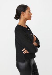 Zwarte gebreide cardigan met een ronde hals en twee gouden knopen, met driekwart mouwen. De stof heeft een getextureerd uiterlijk.