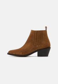Bottes à chevilles en suede marron avec un bout pointu, un petit talon empilé et des accents de couture verticale sur les côtés. Une languette à l'arrière pour un enfilage facile.