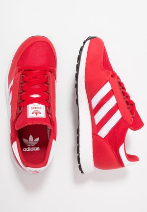 Par de zapatillas Adidas rojas con rayas blancas y suelas negras, mostradas desde arriba y de lado sobre un fondo blanco.