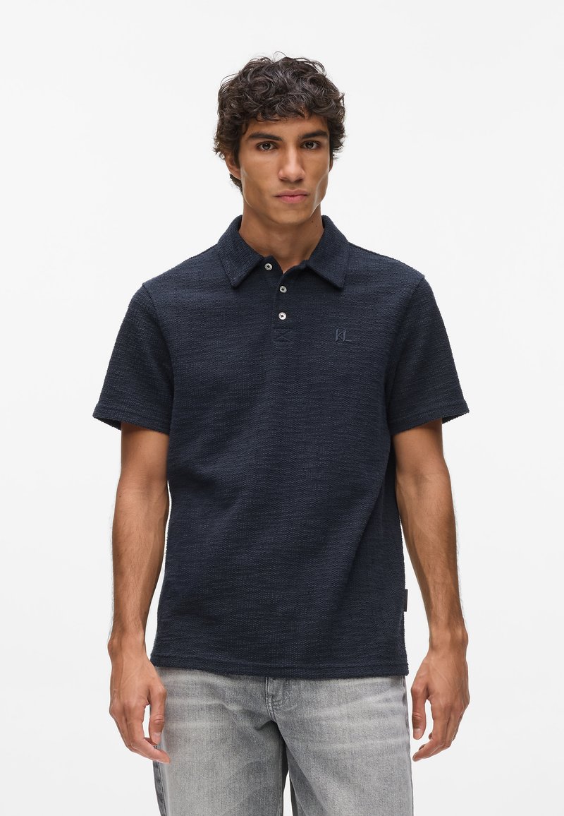 Granatowa koszulka polo z teksturowanej tkaniny, krótki rękaw i kołnierzyk. Posiada dwie guziki i małe logo na piersi.