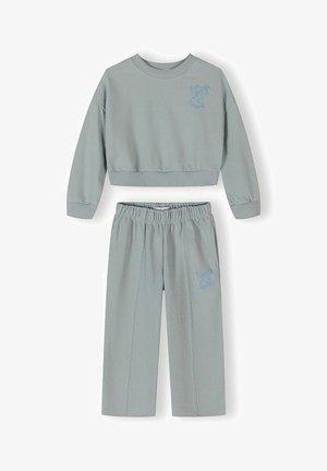 Világosszürke kétdarabos szett, hosszú ujjú, rövidített pulóverrel és magas derekú nadrággal, mindkettőn kék masni hímzés található a bal oldalon.