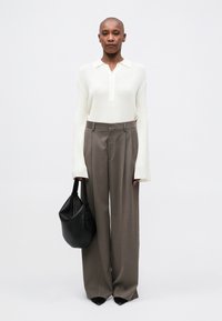 Polo shirt bianco a costine a maniche lunghe, pantaloni grigi a vita alta e una borsa nera con texture. Scarpe nere a punta completano il look.