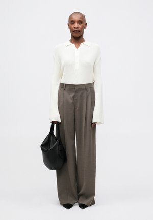 Polo shirt bianco a costine a maniche lunghe, pantaloni grigi a vita alta e una borsa nera con texture. Scarpe nere a punta completano il look.