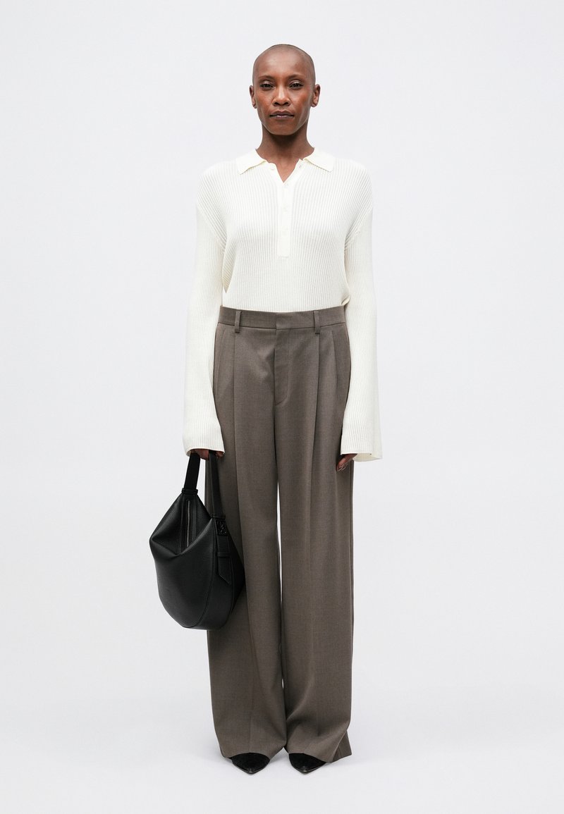 Polo shirt bianco a costine a maniche lunghe, pantaloni grigi a vita alta e una borsa nera con texture. Scarpe nere a punta completano il look.