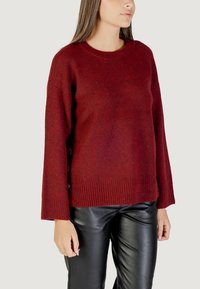 Maglione a maglia bordeaux con orlo e polsini a costine; presenta dettagli con bottoni laterali. Abbinato a pantaloni in pelle nera. Texture morbida e vestibilità comoda.