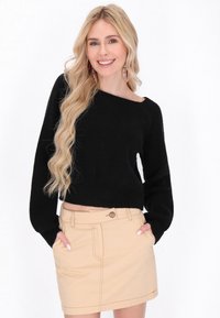 Fekete, rövidített pulóver bordás textúrával és széles ujjak kialakítással, bézs mini szoknyával párosítva, amely elülső zsebekkel és gombos részlettel rendelkezik.