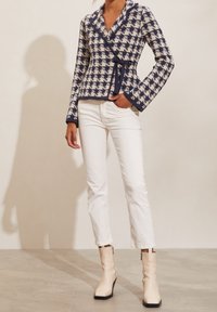 Marinblå och krämfärgad hounds-tooth omslagjacka med knyt, långa ärmar och sjalkrage, tillsammans med vita raka jeans och beige ankelskots.