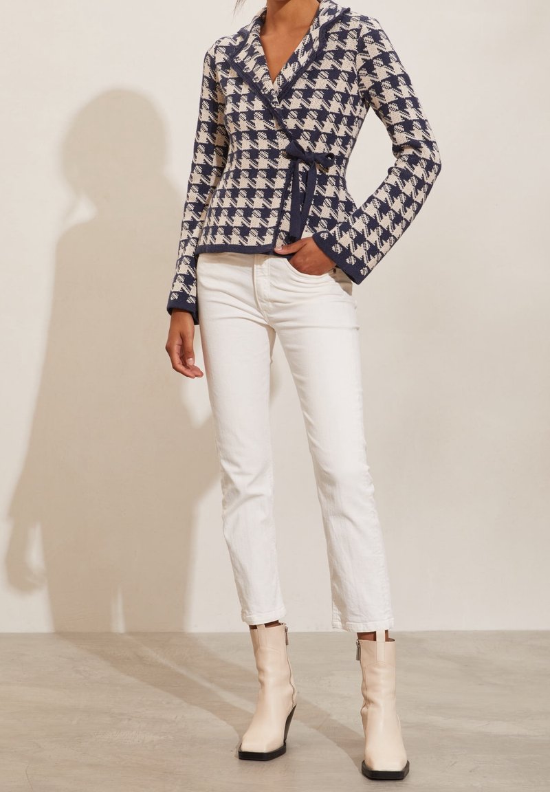 Marinblå och krämfärgad hounds-tooth omslagjacka med knyt, långa ärmar och sjalkrage, tillsammans med vita raka jeans och beige ankelskots.