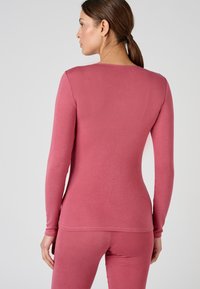 Top a maniche lunghe in morbido tessuto rosa con design aderente. Presenta un collo rotondo e una texture liscia, abbinato a leggings coordinati.