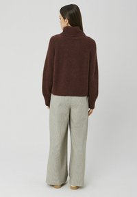 Pull bordeaux avec un col montant, ourlet côtelé et coupe ample, associé à un pantalon large à carreaux beige. Texture douce et design décontracté.