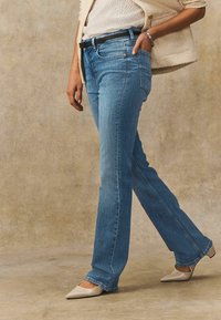 Ljusblå raka jeans i denim, med femficksdesign, subtila slitningar och sliten fåll, som bärs med beige klackar.