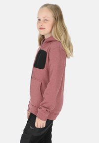 Ritsvest in gemêleerde rozenkleur met een zwart borstzakje. Heeft een comfortabele pasvorm en een zachte textuur. Gecombineerd met zwarte broek.