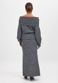 Grauer gestrickter Off-Shoulder-Pullover mit einem strukturierten Design, kombiniert mit einem passenden langen Rock. Beide bestehen aus einem weichen, warmen Stoff. Braune Absätze runden das Outfit ab.