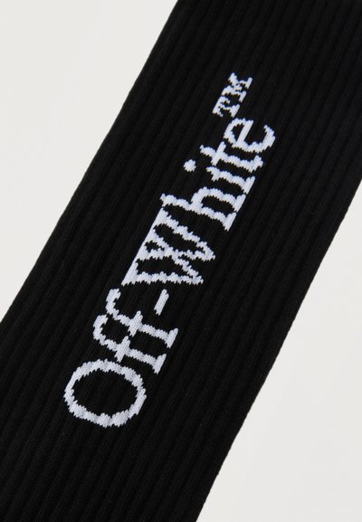 Tissu noir côtelé avec un texte blanc tricoté "Off-White TM" affiché en diagonale sur le matériau.