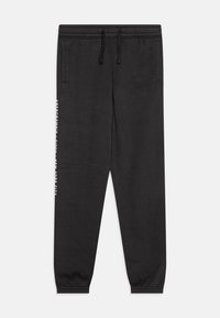 Schwarze Baumwoll-Jogginghosen mit elastischem Bund und Bündchen. Mit Seitentaschen und weißen Textdetails am linken Bein.