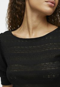 Top negru texturat, cu un decolteu larg, mâneci scurte tip puff și un design tricotat cu model de dungi orizontale.