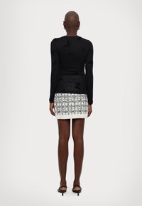 Haut à manches longues noir avec motif de papillons, associé à une mini-jupe à carreaux texturée blanche et grise. Coupe ajustée et longueur au genou.