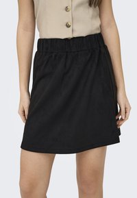 Svart skinnminiskjørt med elastisk midjebånd, har en jevn tekstur og enkel A-linje form. Ingen synlige mønstre eller detaljer.