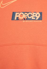 Sudadera naranja con un gráfico azul que dice "FORCE9" y "por Erling Haaland", con un ligero logotipo de Nike en la parte superior.