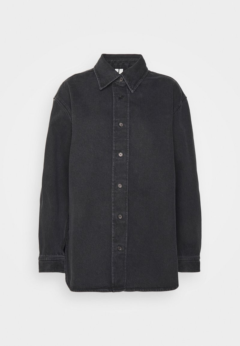 Chemise noire à manches longues avec boutons, col classique et coutures visibles sur les coutures, sur un fond uni.