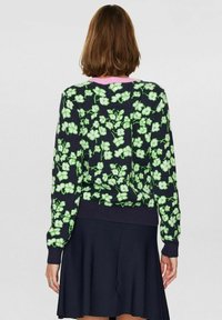 Granatowy sweter z dzianiny z zielonym kwiatowym wzorem, ściągaczami przy mankietach i dole oraz różowym dekoltem. Noszony z czarną rozkloszowaną spódnicą.