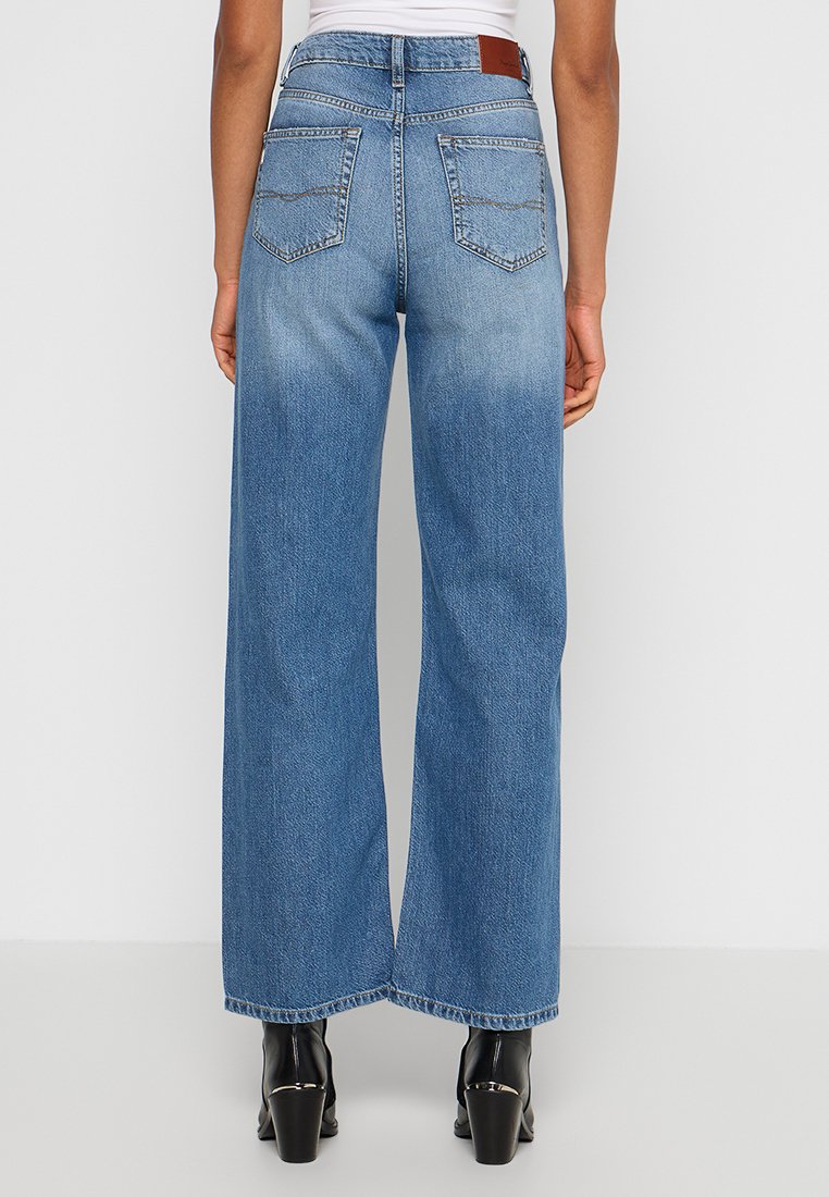 Szerokie niebieskie dżinsy z denimowym wykończeniem, z pięcioma kieszeniami i skórzaną metką w pasie. Gładka tekstura i prosty krój.