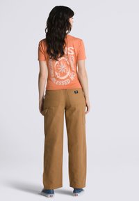 Orange graphic t-shirt with white print, paired with loose-fitting, tan wide-leg trousers, featuring side pockets and visible stitching details.