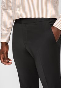 Svarta kostymbyxor med en slät yta och skräddarsydd passform. Kombineras med en randig skjorta i beige och vitt som visar upp en klassisk design.