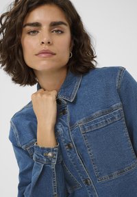 Vidēji zilā denima jaka ar pogājamām priekšējām daļām, krūšu kabatu un izšuvumiem. Mīksta tekstūra ar strukturētu dizainu.